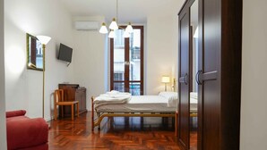 A hotel room with a bed, a red chair, a wooden dresser, a TV, and a window with a view of buildings. - Neapolitan Soul 3 By Dimorra (Napoli)