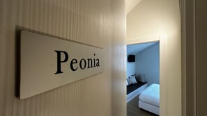 A hotel room with a bed, a TV, and a sign on the wall that reads "Peonia".