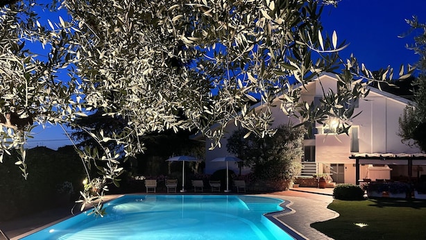 Ein Swimmingpool mit glasklarer, blauer Wasseroberfläche, umgeben von einer gepflasterten Liegefläche und einem gepflegten Rasen.