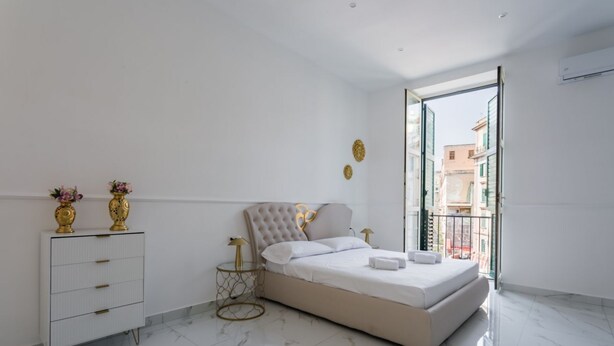 A modern bedroom with a large bed, a white dresser, and a small side table. - Golden Suites Golden room by Dimorra (NAPOLI)