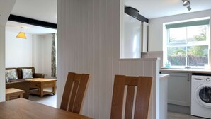 Une cuisine moderne équipée d’un lave-linge, un coin repas avec une table et des chaises en bois, et une vue sur l’extérieur par une fenêtre.