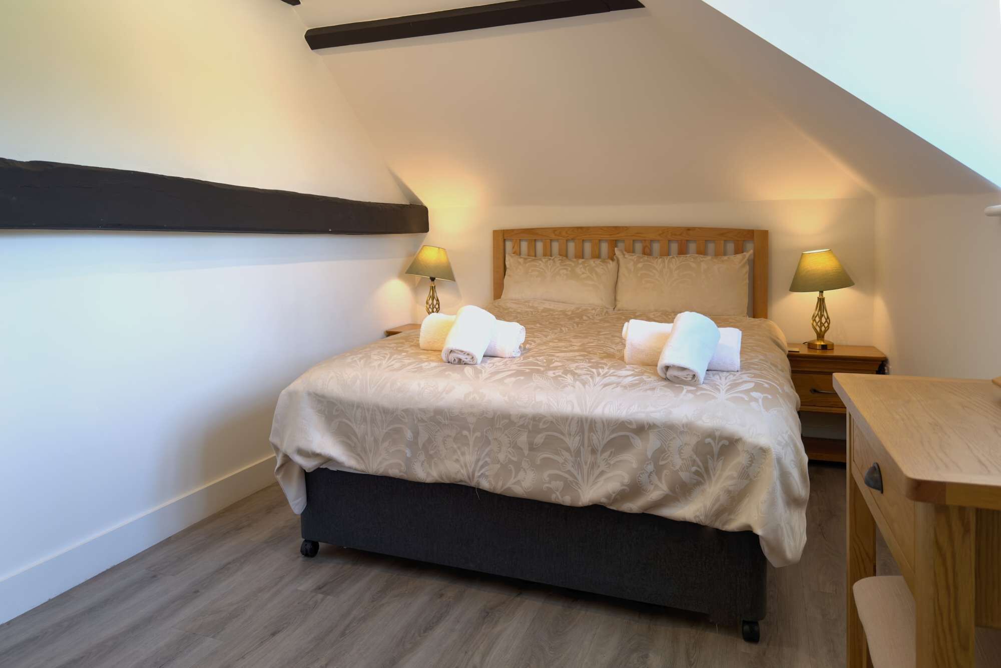 A bedroom with a bed, two bedside lamps, a wooden nightstand, and a small table.