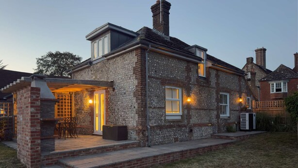 Une maison à deux étages avec une façade en pierre, un patio couvert avec des meubles d’extérieur et une cheminée.
