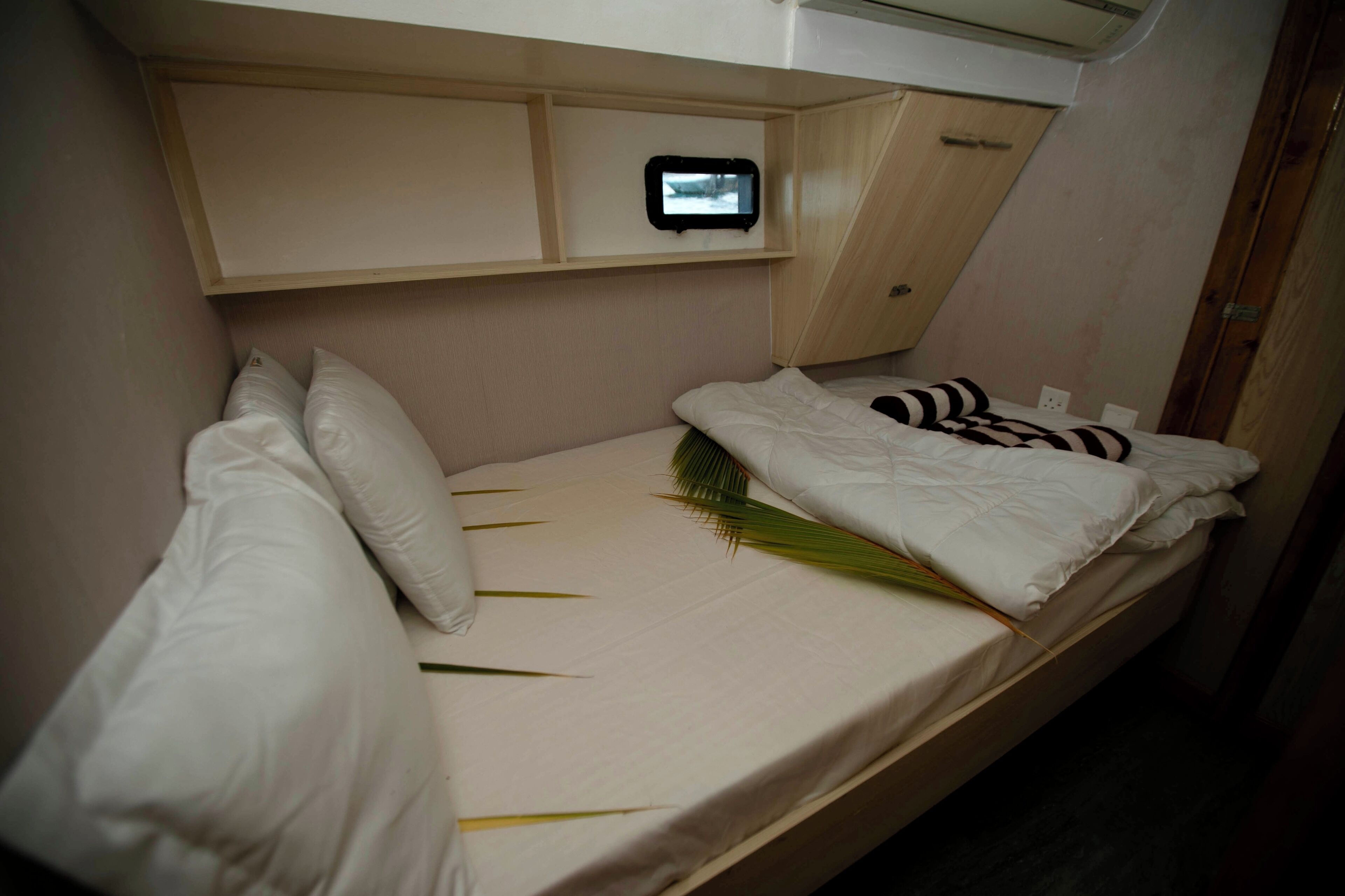 Una cama individual con ropa de cama blanca y un pequeño dispositivo fijado en la pared de arriba.