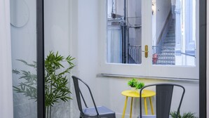 Una habitació amb una finestra gran, una taula petita groga, dues cadires i una planta en test.