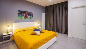 Un dormitori modern amb un llit gran, una petita taula de nit, un televisor fixat a la paret i una porta amb cortines.