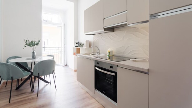 A modern kitchen with a built-in oven, a stainless steel range hood, and a small dining area with a round table and two chairs. - Metro Station By Dimorra (Napoli)