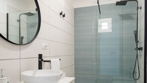 A modern bathroom with a large white sink, a round mirror, and a glass-enclosed shower area. - Metro Station By Dimorra (Napoli)