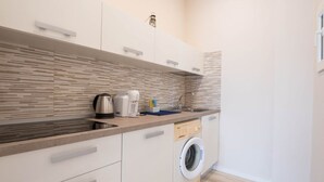 Une cuisine compacte équipée d’un lave-linge intégré, d’une machine à café et d’une bouilloire.