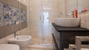 Une salle de bain moderne avec une douche à l’italienne en verre, un lavabo blanc et un bidet.