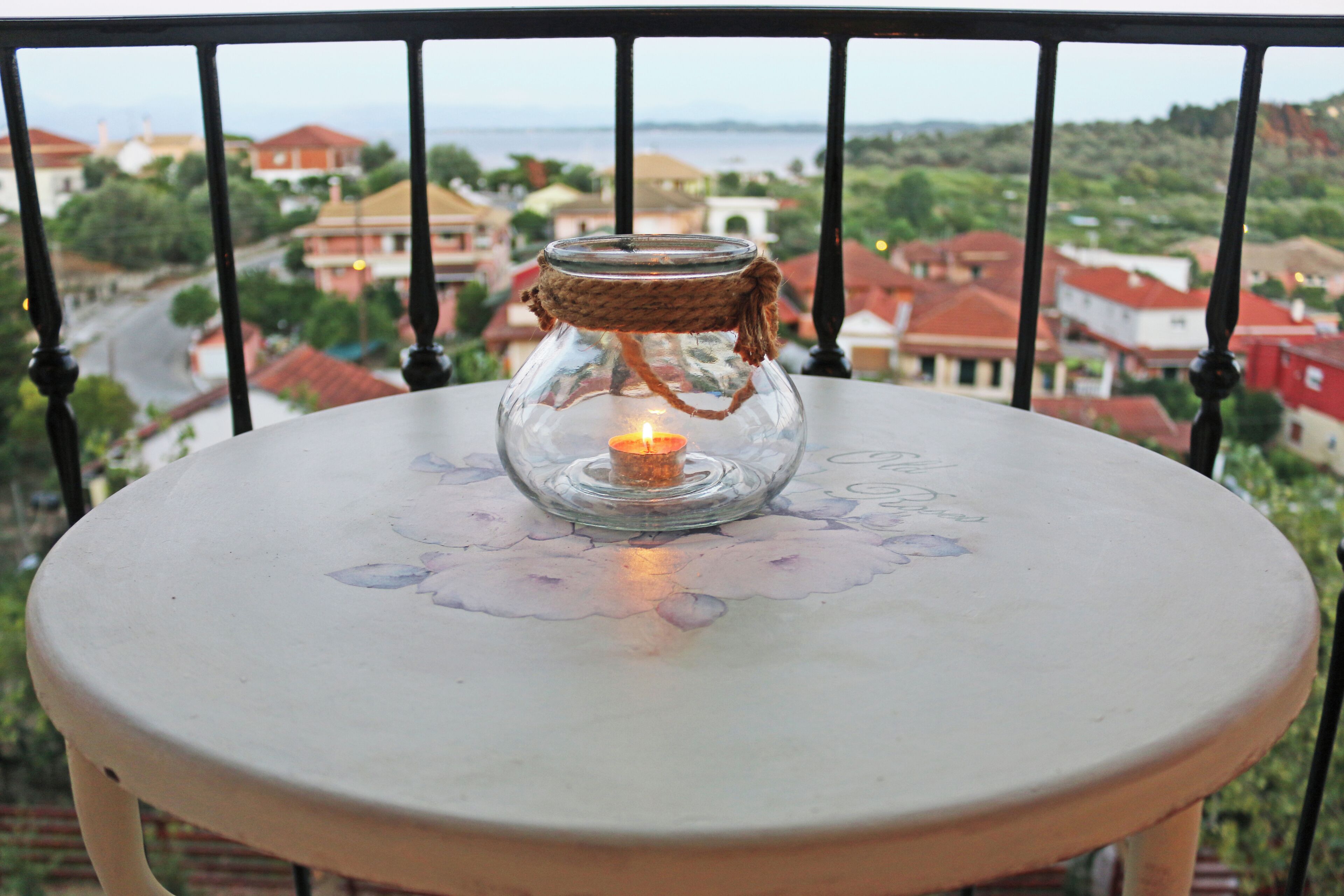 Una mesa con una vela, ubicada en un balcón con vista a casas y una carretera.
