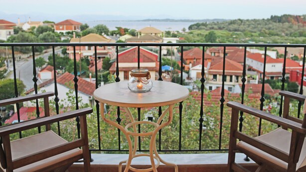 Un balcon avec une table ronde et deux chaises, donnant sur un quartier résidentiel avec des maisons aux toits rouges et de la verdure.