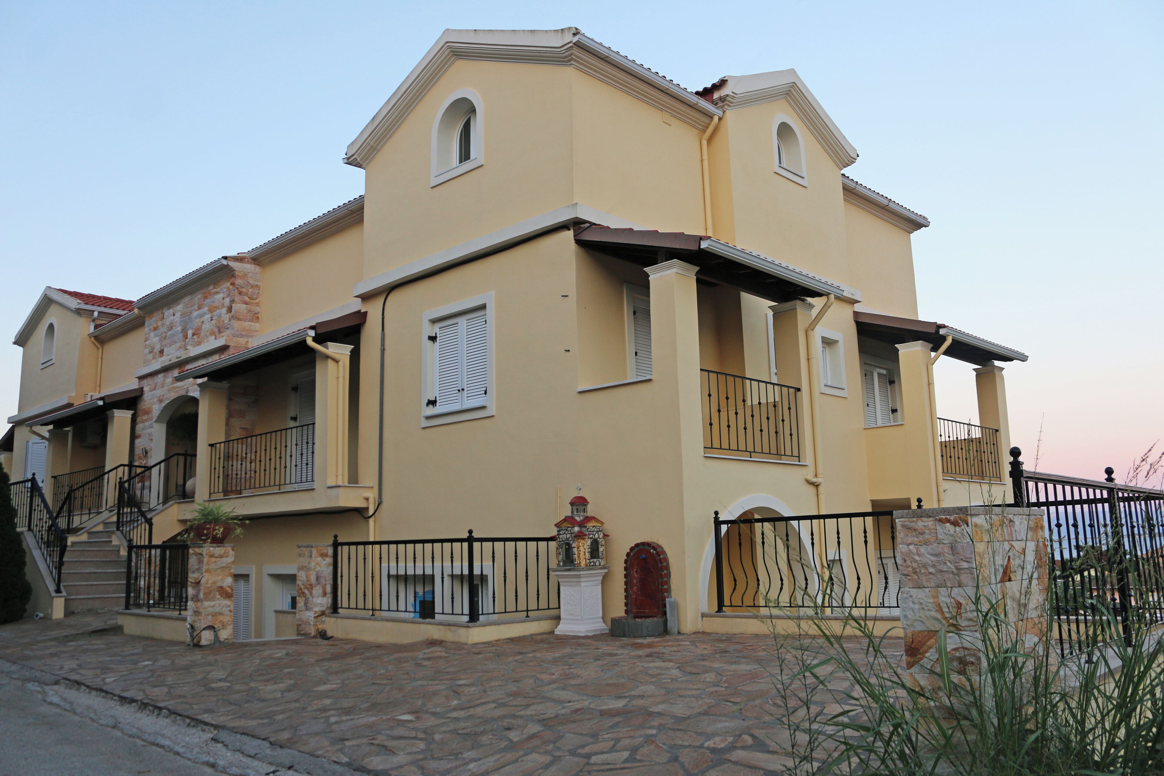 A two-story building with a stone facade, a balcony, and a small statue in front.