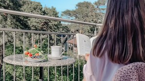 A person reading a book at a round table with a white cup and saucer, a plate with food, and a small potted plant. - Beautiful apartment in Pobierowo with WiFi (Pobierowo)