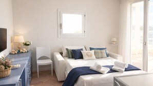Et hotelværelse med en seng, et skrivebord med lampe, en stol, et fjernsyn og et vindue.