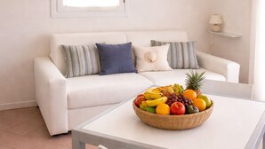 En hvid sofa med stribede puder, et hvidt bord med en skål med frugt og en lampe på en hylde.