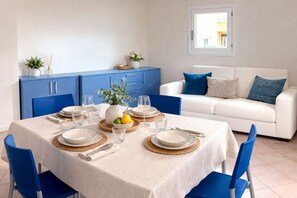 A dining area with a table set for four, blue chairs, a white sofa with blue cushions, and a blue cabinet.