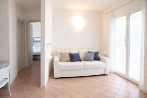 A white sofa with patterned cushions, a tiled floor, and a sliding glass door.