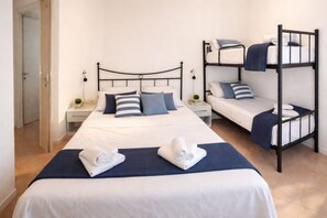 A hotel room with a single bed, a bunk bed, a bedside table with a lamp, and a small plant.