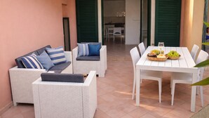 A patio area with wicker furniture, a dining table with fruit, and a kitchen in the background. - Li Velieri 6 pax Pool & Private Garden (Santa Teresa Gallura)