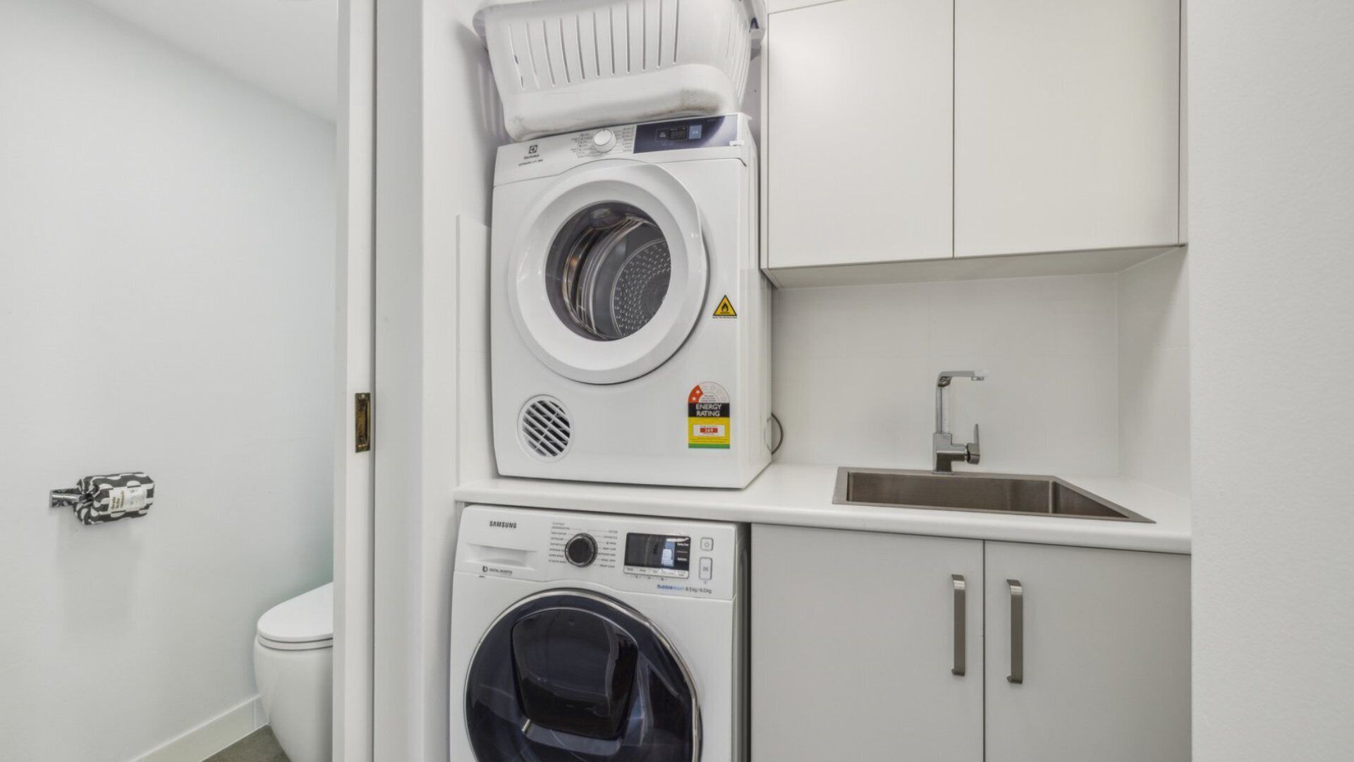 A compact laundry room with a front-loading washer and dryer, a small sink, and a cabinet.