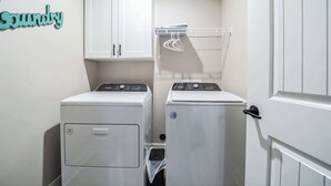 A laundry room with two front-loading washing machines, a drying rack, and a cabinet labeled "Laundry". - Serene 2-Bedroom Condo in Traverse City (Williamsburg)