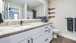 A bathroom with a granite countertop, a white toilet, and a shower with a curtain. - Serene 2-Bedroom Condo in Traverse City (Williamsburg)