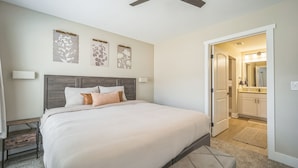 Un dormitorio con cama, ventilador de techo y puerta que da a un baño.