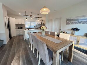 A modern kitchen with white cabinets, a wooden dining table, and a hanging light fixture. - River Walk Retreat in Wynyard (Wynyard)
