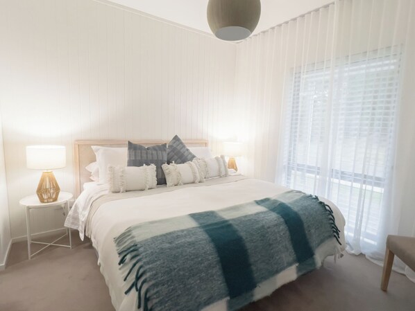 A bedroom with a large bed, two bedside tables, a hanging light fixture, and a window with sheer curtains. - River Walk Retreat in Wynyard (Wynyard)