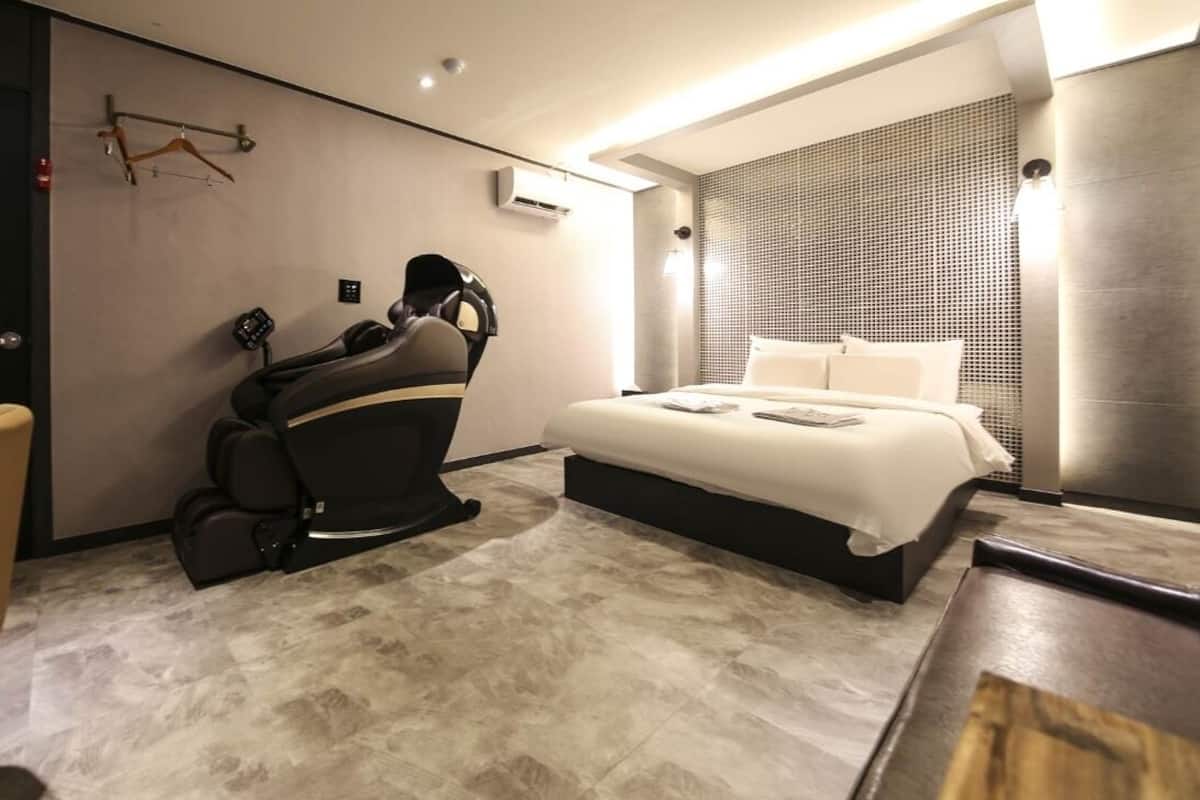Una camera d'albergo moderna con una poltrona massaggiante, un letto e una scrivania con sedia.