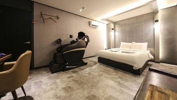 A modern hotel room with a massage chair, a bed, and a desk with a chair.