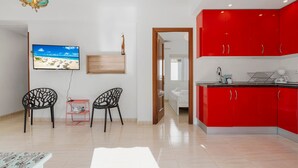 A modern living room with a TV, two chairs, a small table, and a red kitchen area. - Bright Rooftop in Fuengirola City Center by Costarentals - Ref 255 (Fuengirola)