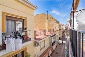 Eine schmale Stadtstraße mit Gebäuden an beiden Seiten, einem Balkon mit Wäsche und einer Person, die vorbeigeht.