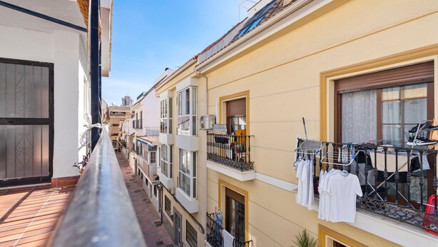 A narrow urban street with multi-story buildings, balconies with laundry hanging, and a clear blue sky. - Bright Rooftop in Fuengirola City Center by Costarentals - Ref 255 (Fuengirola)