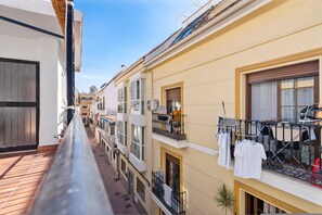 A narrow urban street with multi-story buildings, balconies with laundry hanging, and a clear blue sky. - Bright Rooftop in Fuengirola City Center by Costarentals - Ref 255 (Fuengirola)