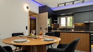 Ein moderner Essbereich mit einem Holztisch, gedeckt für vier Personen, umgeben von schwarzen Stühlen. Im Hintergrund ist eine Küche mit dunklen Schränken und einer eingebauten Kochinsel zu sehen.
