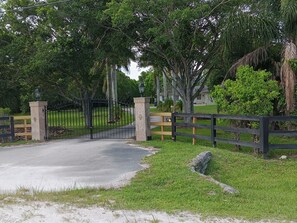 A gated entrance with a paved driveway leading to a grassy area with trees and a wooden fence. - 
Private 5-Acre Retreat in Rustic Ranches with Modern Country Comfort (Wellington)