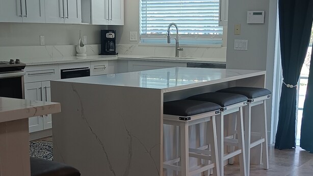 A modern kitchen with white cabinets, a marble countertop, and a built-in island with bar stools. - 
Private 5-Acre Retreat in Rustic Ranches with Modern Country Comfort (Wellington)
