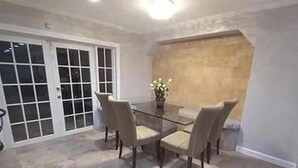 A dining area with a glass table and four chairs, a vase with flowers, and a stone accent wall. - 
Private 5-Acre Retreat in Rustic Ranches with Modern Country Comfort (Wellington)