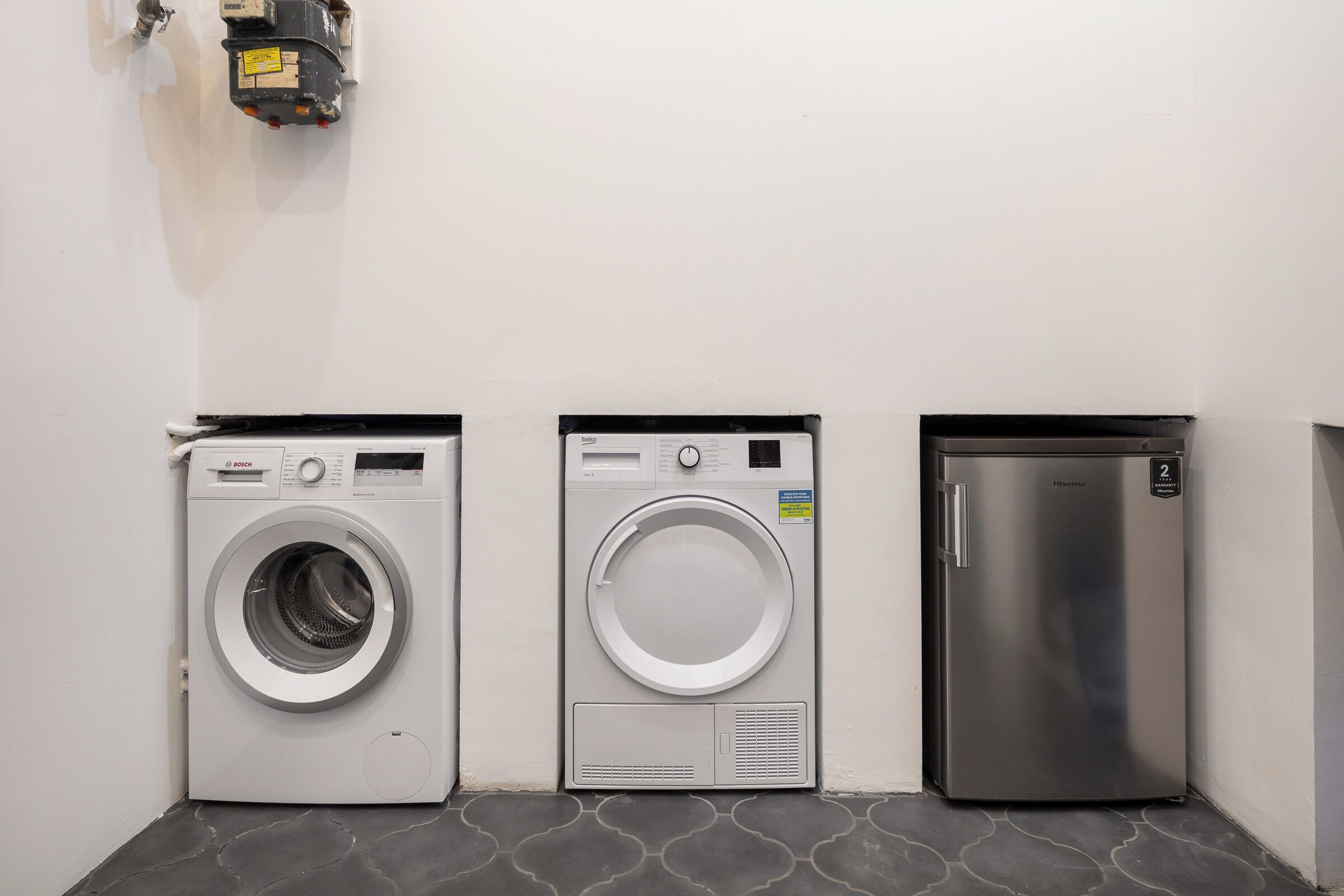A laundry area with a Bosch washing machine, a front-loading dryer, and a stainless steel refrigerator.