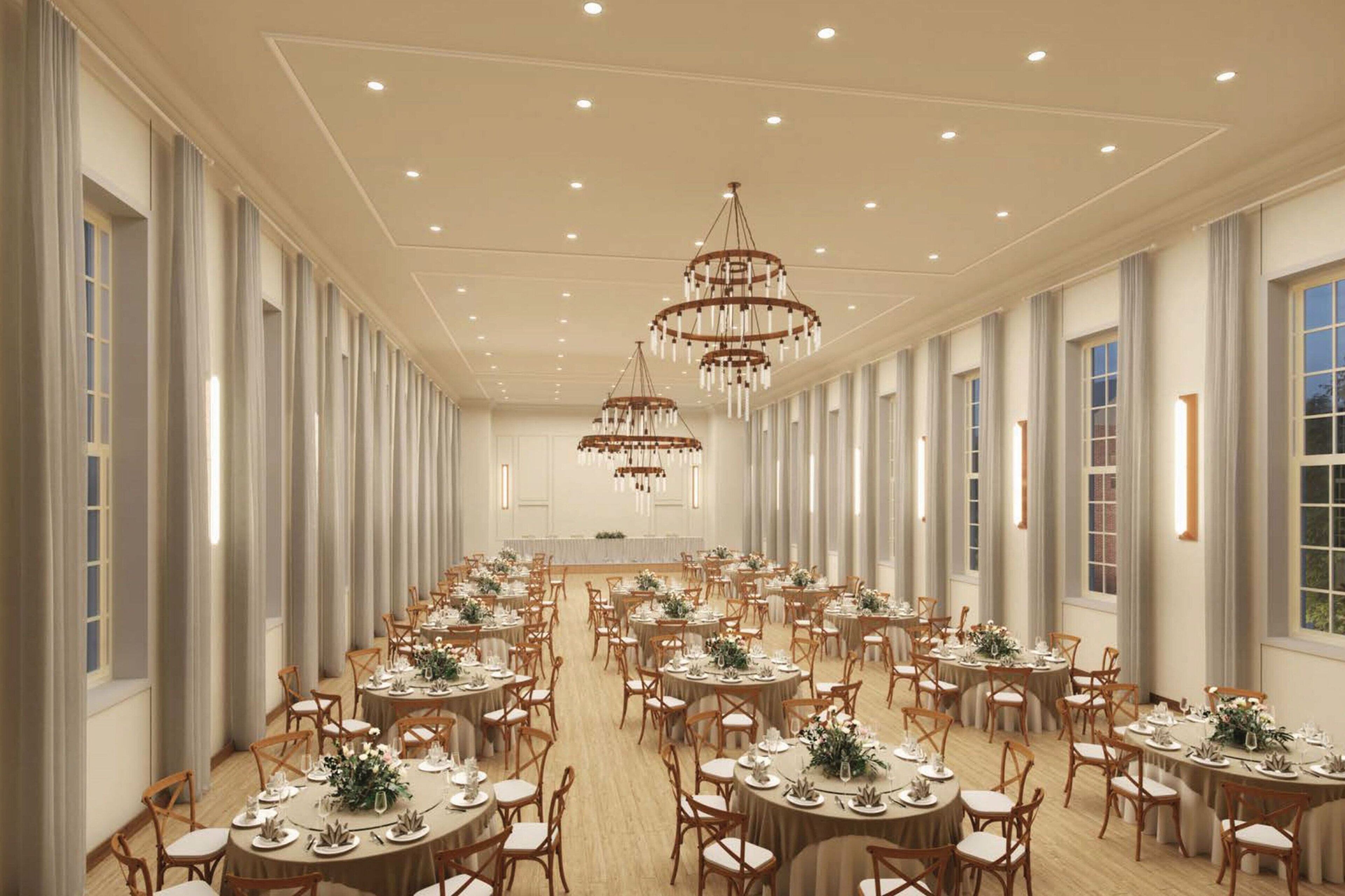 A large banquet hall with round tables, chandeliers, and tall windows.