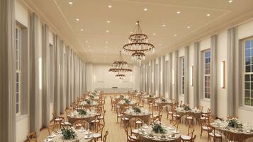 A large banquet hall with round tables, chandeliers, and tall windows.