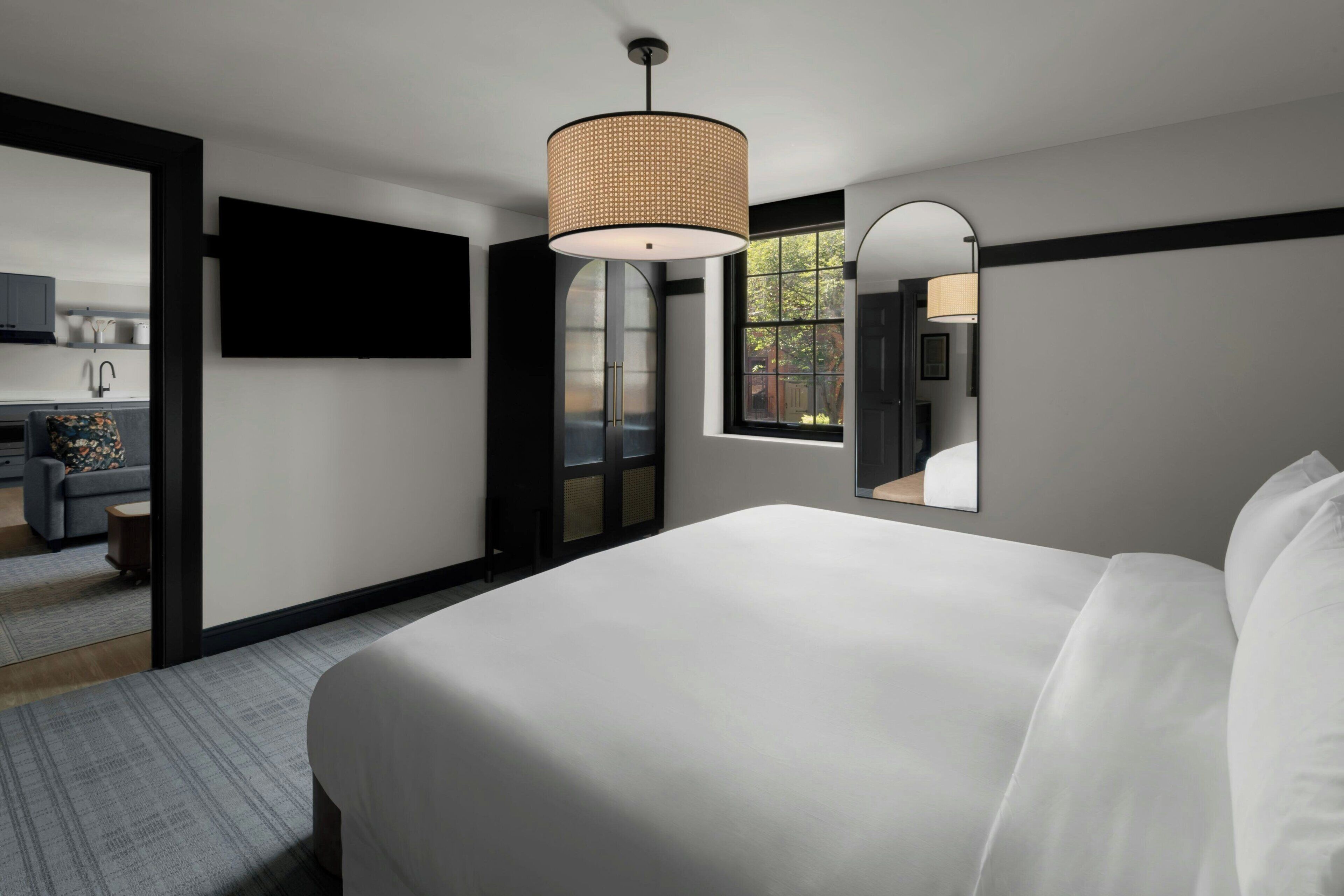 A modern hotel room with a large bed, a flat-screen TV, a dining area, and a view of the outdoors.
