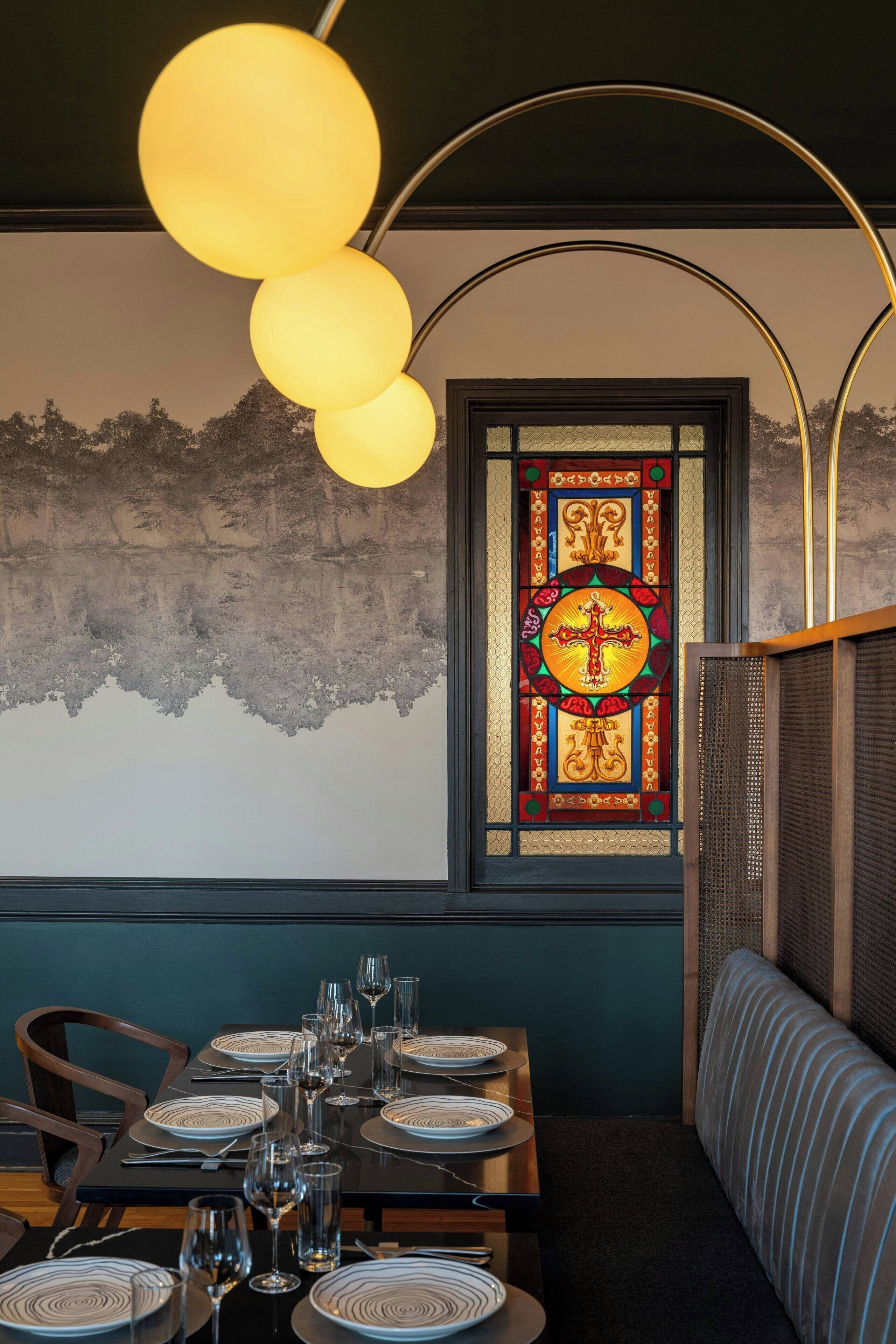 A restaurant interior with a dining table set for six, a decorative stained glass window, and a modern light fixture.