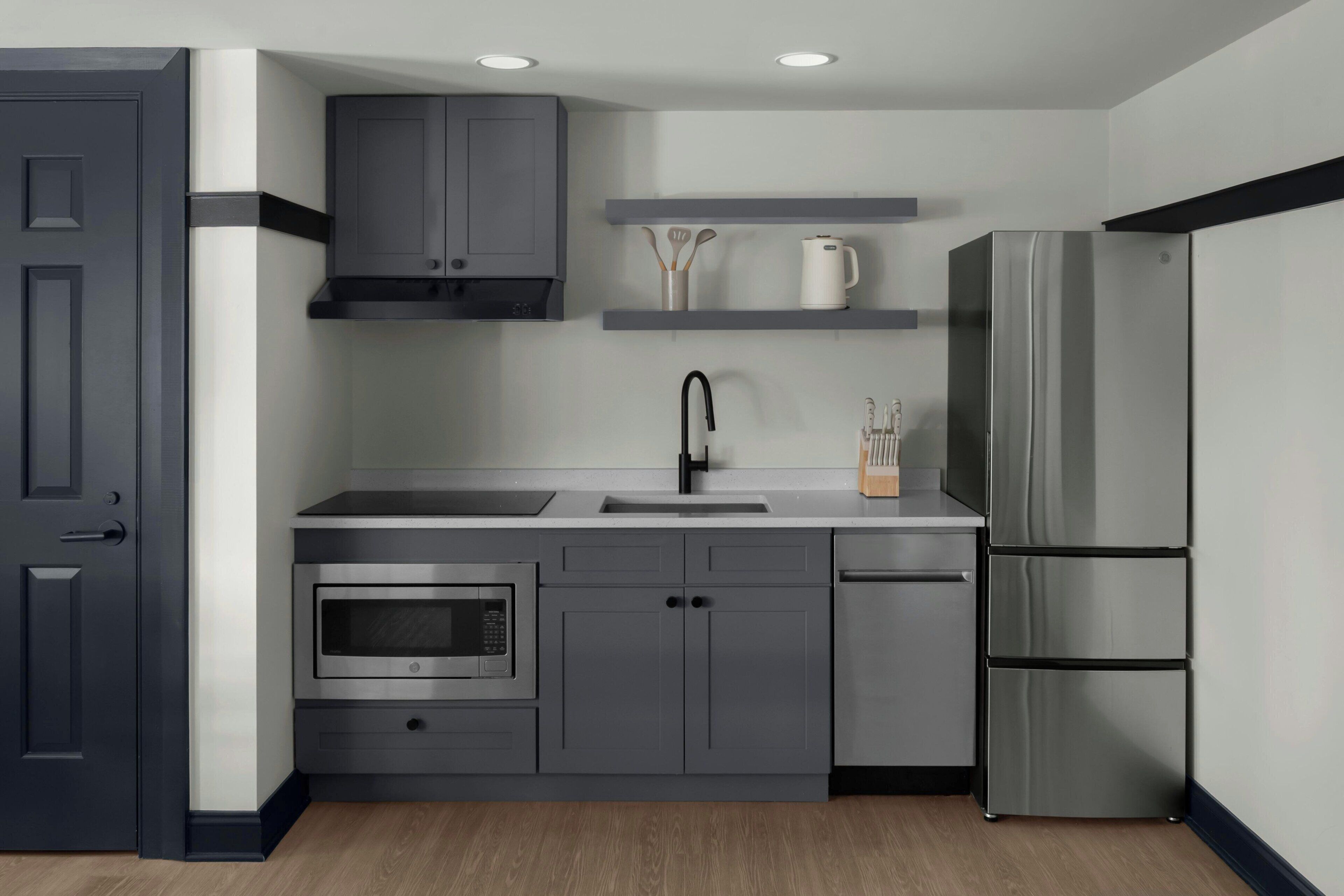 A modern kitchen with grey cabinetry, a stainless steel refrigerator, an oven, and a sink.