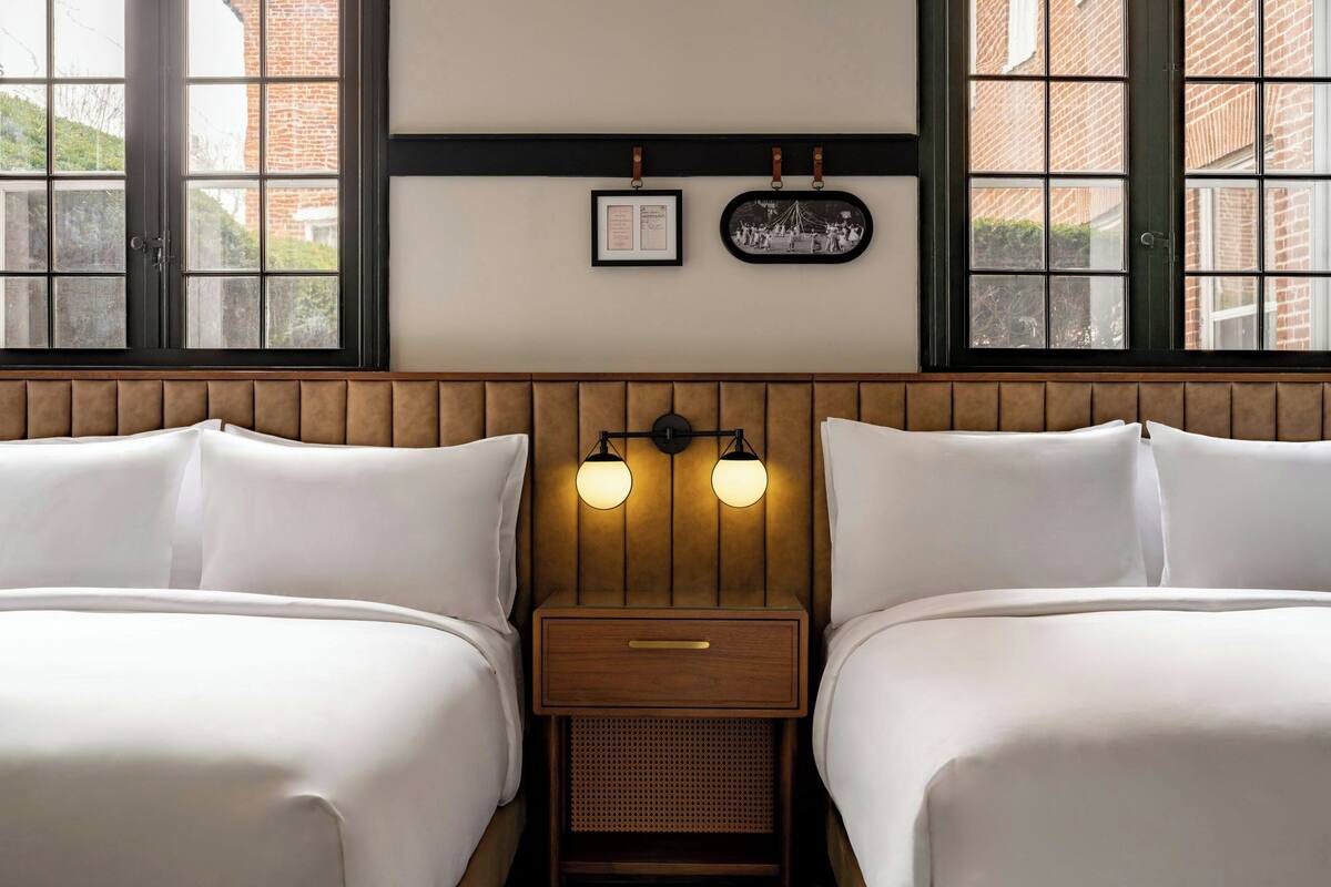 A hotel room with two beds, a wooden headboard, a nightstand with a drawer, and a wall-mounted picture frame.