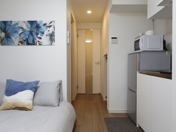 A compact hotel room with a bed, a kitchenette, and a door leading to a bathroom. - BE Terrace Nishi-Shinjuku _Shinjuku Area / 5-minute walk from Nishi-Shinjuku Station, 6 minutes from Shinjuku Station (新宿区)