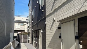 A narrow alleyway between buildings with closed garage doors and a concrete path. - BE Terrace Nishi-Shinjuku _Shinjuku Area / 5 min. walk from Nishi-Shinjuku Station 6 min. from Shinjuku Station (新宿区)
