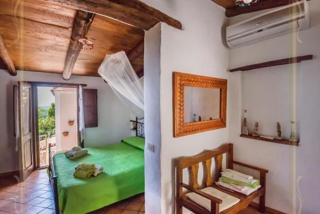 A room with a bed, a wooden chair, a mirror, and a shelf with decorative items.